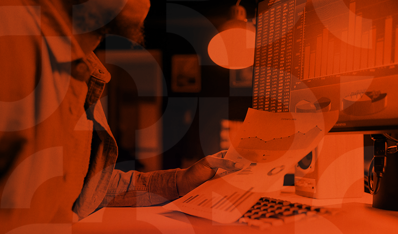 Pessoa analisando dados financeiros em um escritório, com foco em gráficos e relatórios, em ambiente de trabalho moderno.